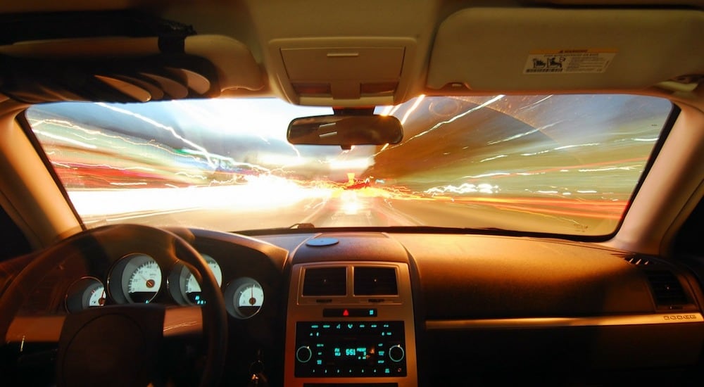 View from inside a car during night driving, showing streaks of colorful traffic lights through the windshield, with a dashboard and steering wheel visible; Montgomery County Traffic Ticket Lawyer concept image
