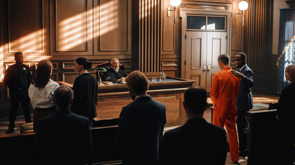 man in orange jumpsuit with lawyer standing in full courtroom