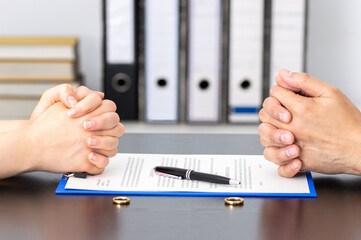 couple with folded hands sitting with rings and divorce agreement